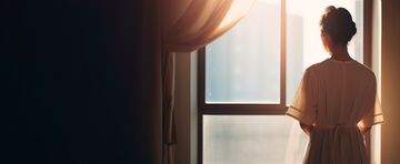 trauernde Frau steht am Fenster